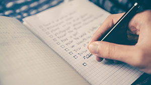 A hand holding a pen, writing a list in a notebook.