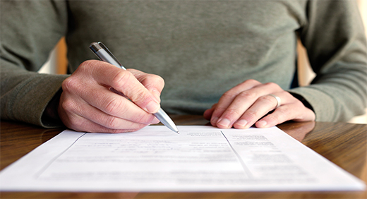 A person in a grey jumper writing with paper and pen on a desk.