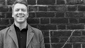 Black and white photograph of Anthony Cartwright standing against a brick wall with the corner of a football goalpost drawn in chalk visible next to him