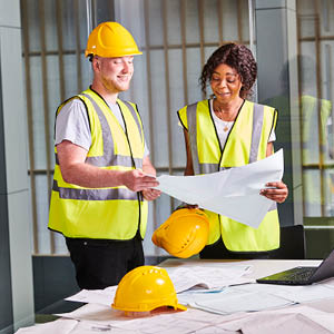 2 students in High vis and hard hats looking at blue prints.