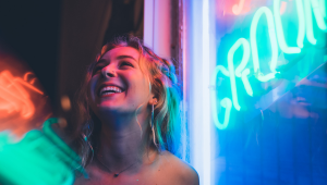 A woman standing by a large window in the light of a neon sign at night