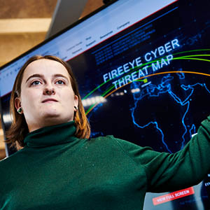Student stood in front of interactive display, that is showing a global cyber attack on screen.