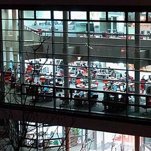 Exterior of a building at night, its many windows illuminated where several floors of busy computer labs are visible.