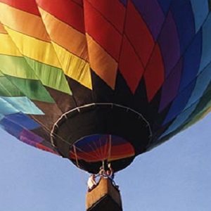A hot air balloon decorated in rainbow diamond patterns flying against a blue sky.