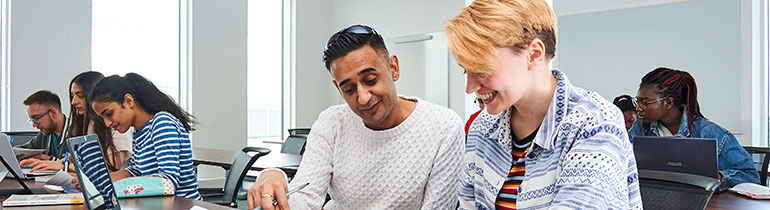 Students in a lecture room taking notes on laptops and pads of paper