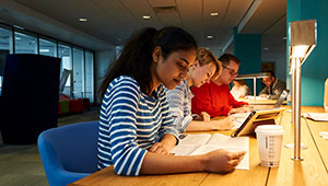 Students sitting at a desk writing on paper under a desk lamp.