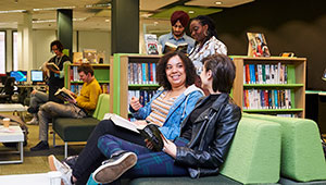 Students in the library on City Campus, sitting together and reading while other students stand around bookshelves