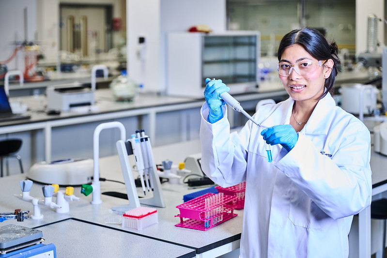 Student in lab coat holding test tube sample